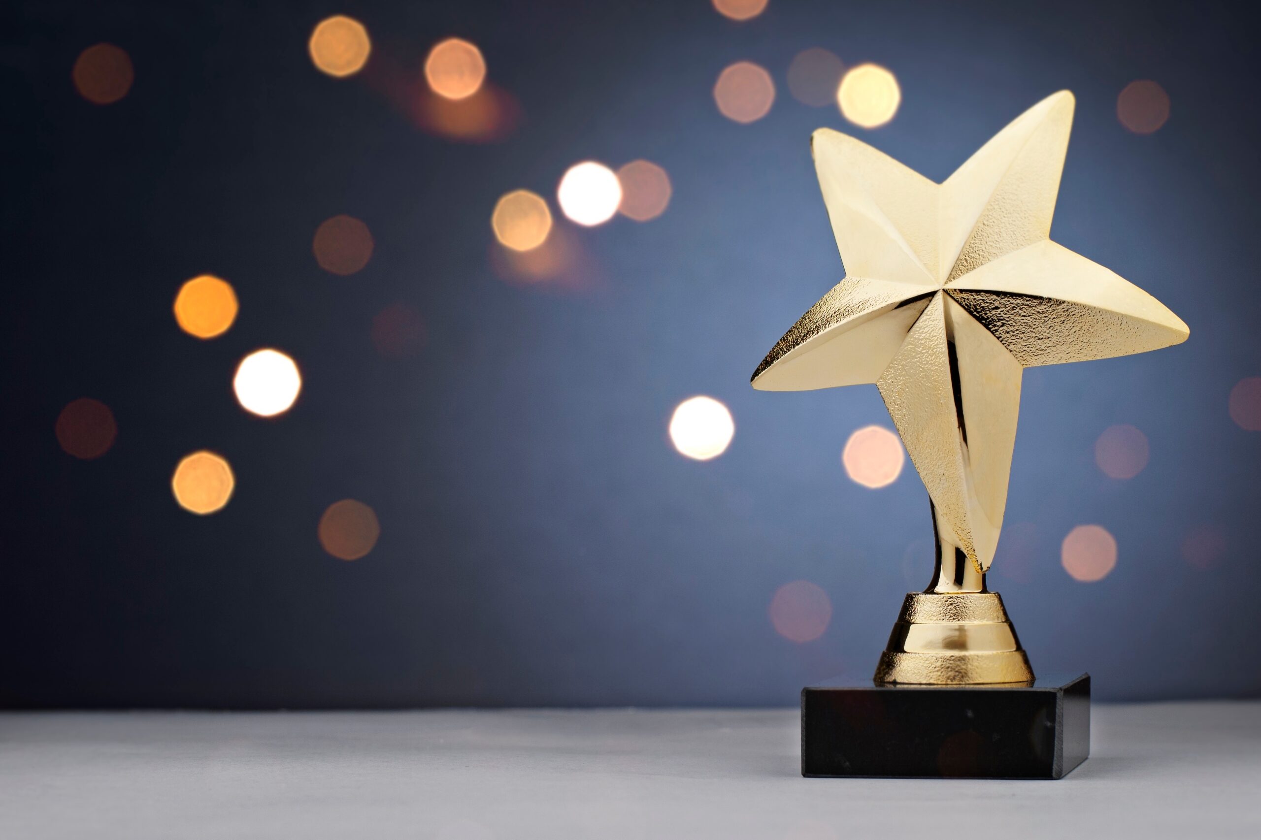 Gold star trophy for a winner or champion of a competition or sporting event placed to the side against a bokeh of sparkling lights with copy space